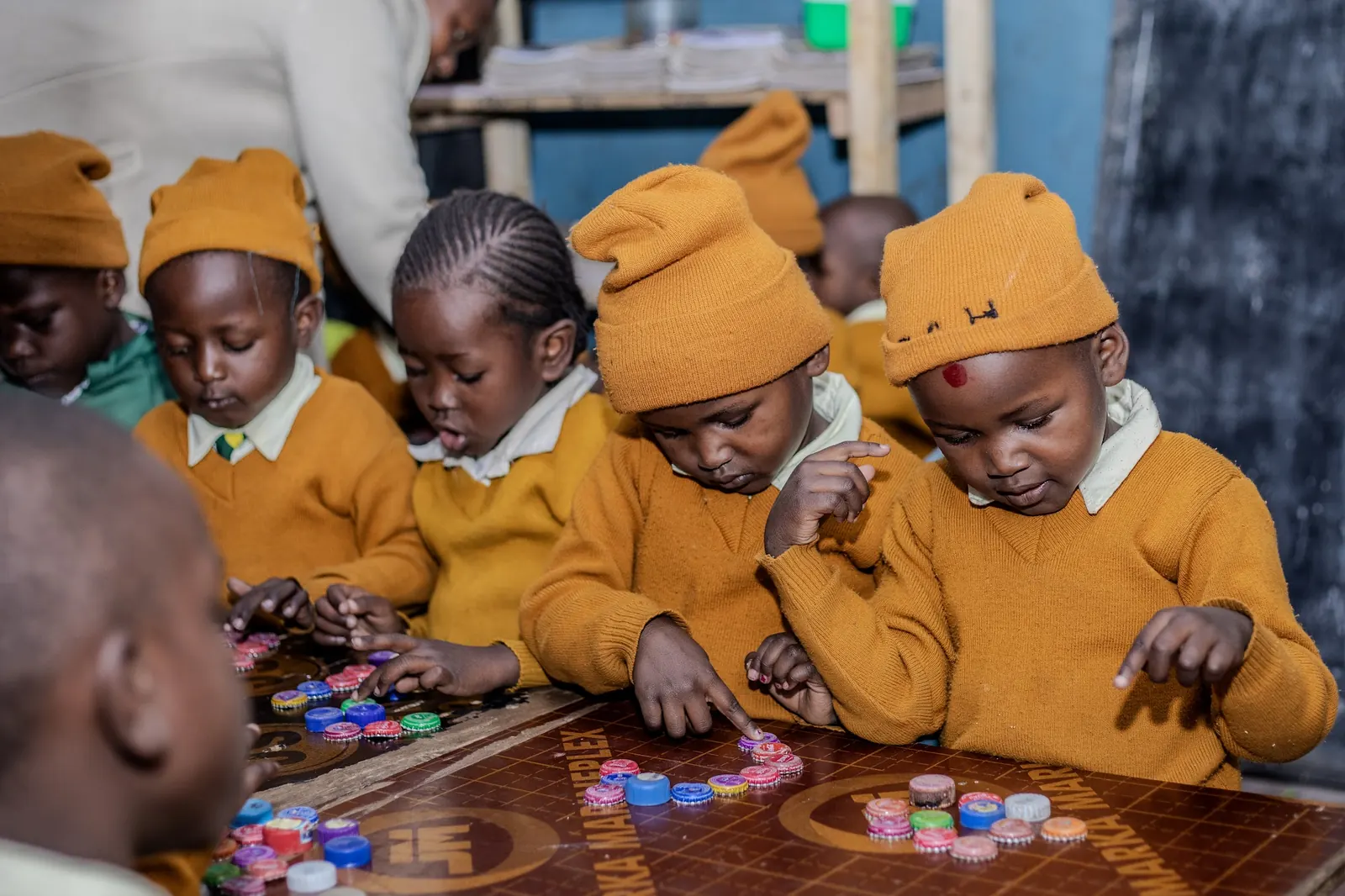 Children in knitted hats counting colourful bottle tops at their table