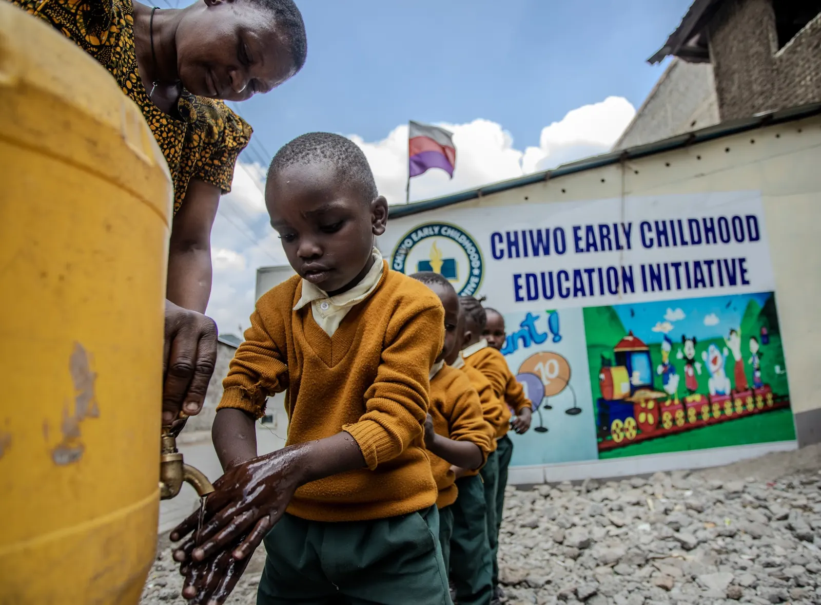 A boy washing his hands at the water tap outside the school