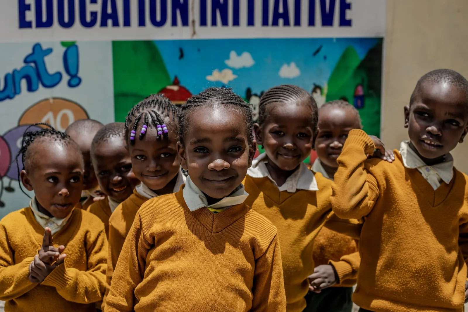 A group of smiling children in front of the school's colourful mural
