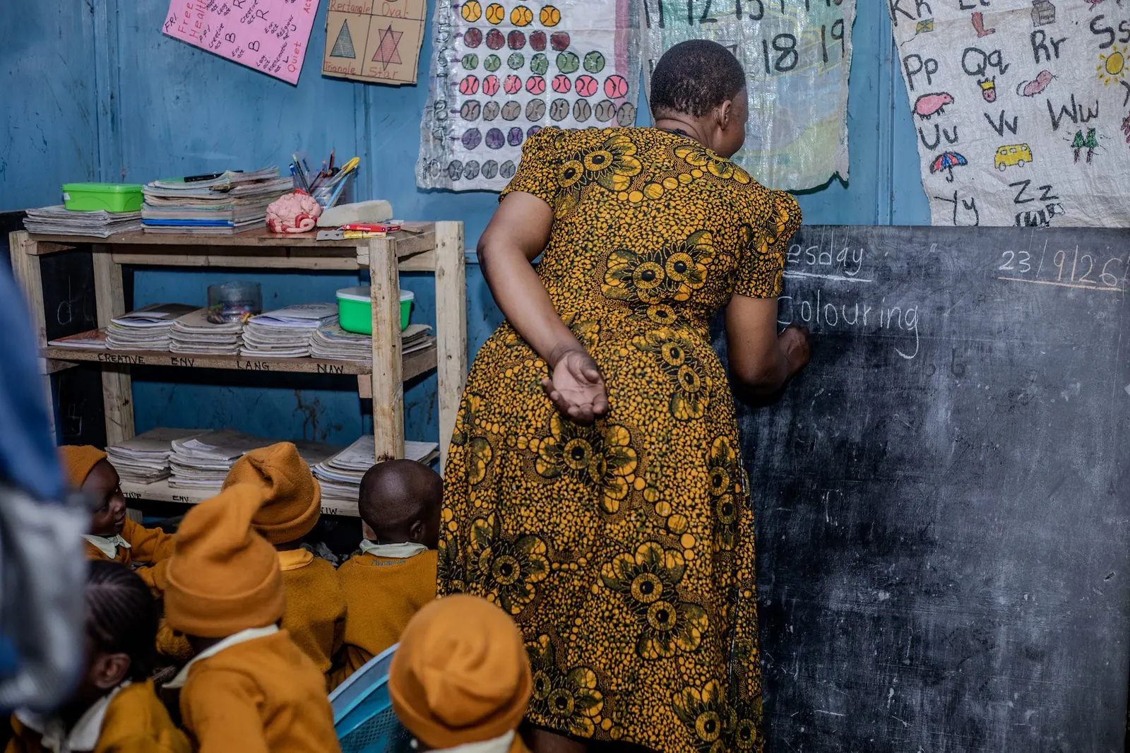 A teacher writing on the chalkboard as children watch