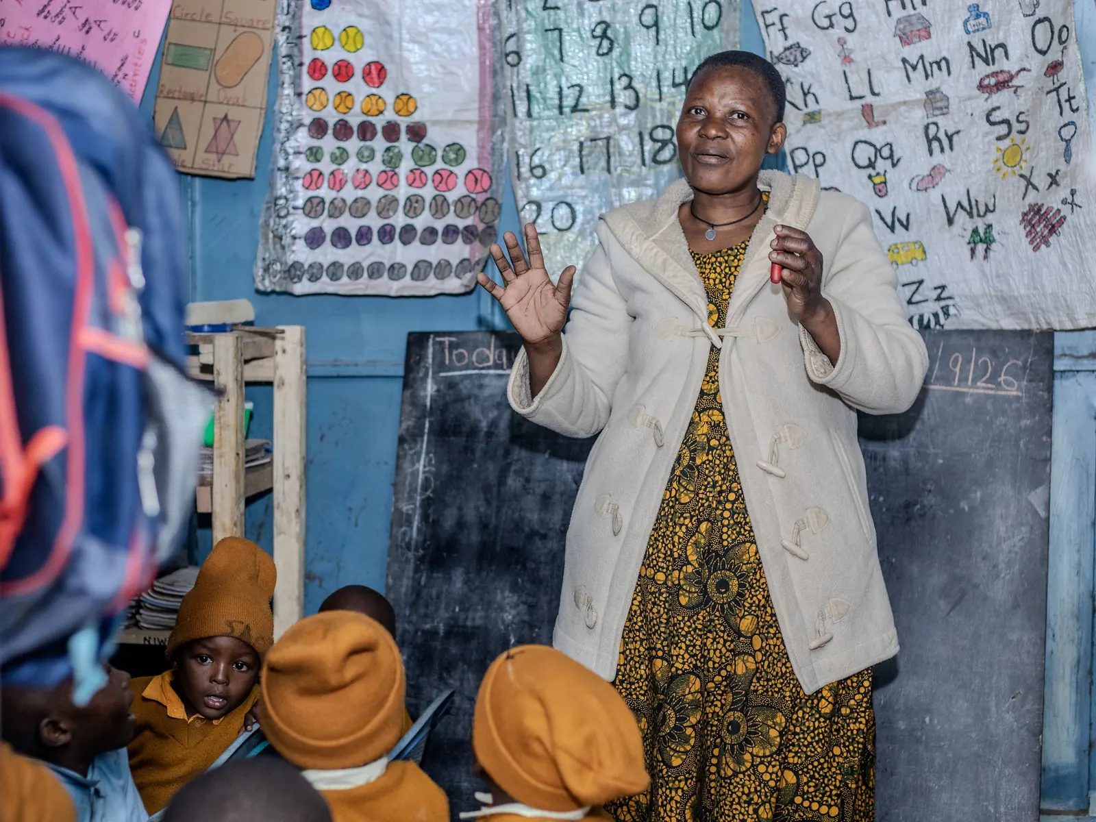 A teacher leading a lesson in front of number and alphabet charts